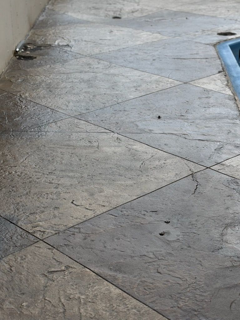 Textured stone patio beside a swimming pool, lit by warm sunlight.