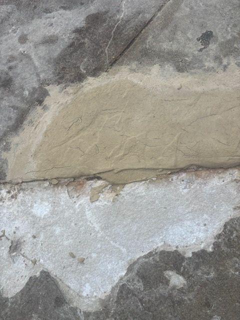 Close-up of a rough stone wall with a tan repaired patch over a white plaster area