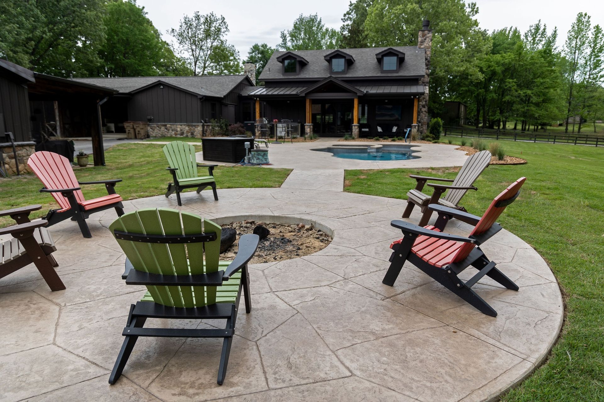 Outdoor patio with colorful Adirondack chairs around fire pits in front of a house