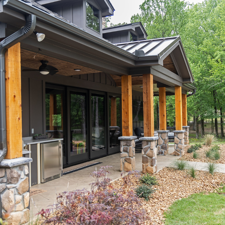 Modern house porch with stone columns, wood posts, glass doors, and landscaped garden beds
