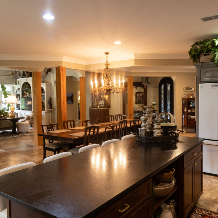 Warm, elegant dining room with long wooden table, chandelier, and dark kitchen island in foreground