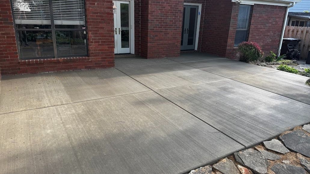 Concrete patio beside a brick house with windows and a stone walkway edge