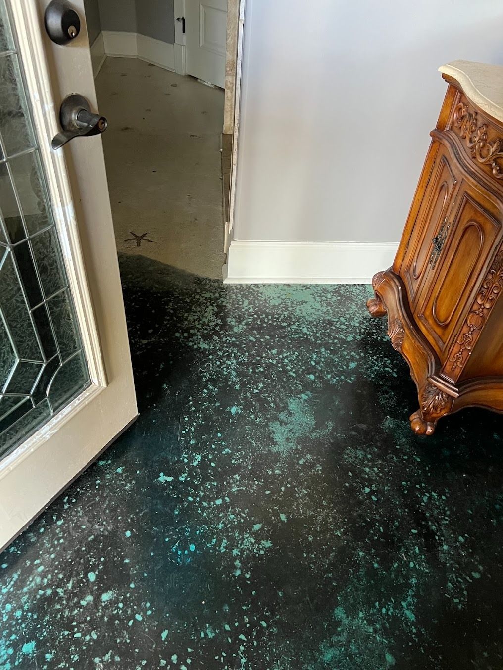 Open front door with shattered glass on the floor beside a hallway and wooden cabinet.