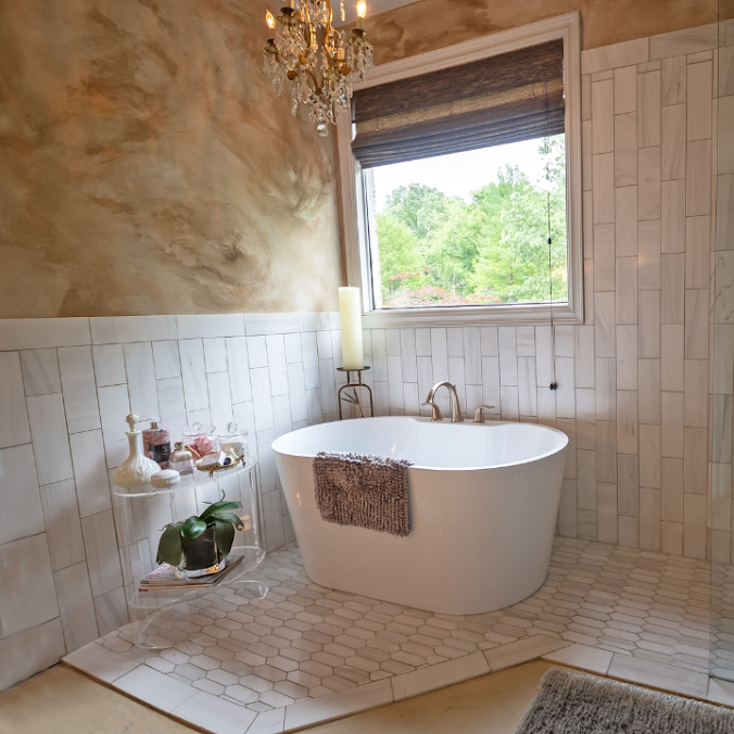 Bright bathroom with freestanding tub, tiled walls, chandelier, and window overlooking greenery