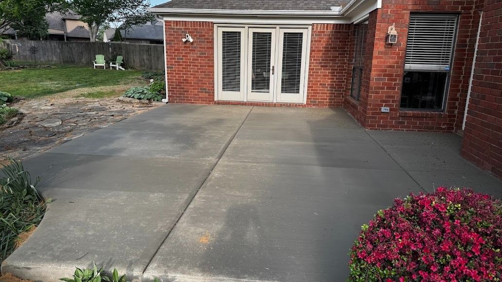 Concrete patio beside a brick house with white French doors and pink flowers in the foreground