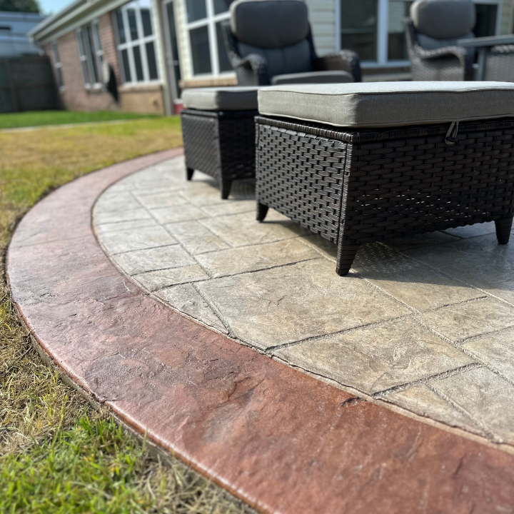 Patio seating with black wicker chairs and ottomans on a curved stone terrace beside a lawn.