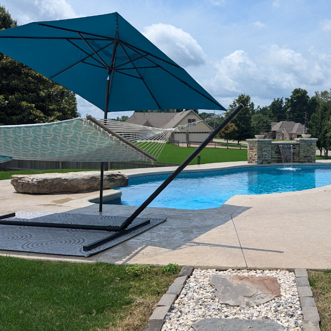 Backyard pool with a large blue umbrella, lounge chair, and clear water on a sunny day