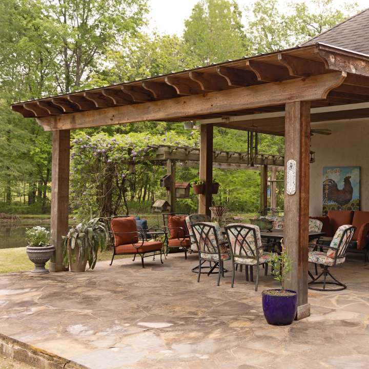 Patio with pergola, outdoor seating, potted plants, and a stone floor surrounded by trees