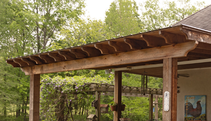 Rustic wooden pergola with a slatted roof surrounded by green trees and shrubs in a garden setting