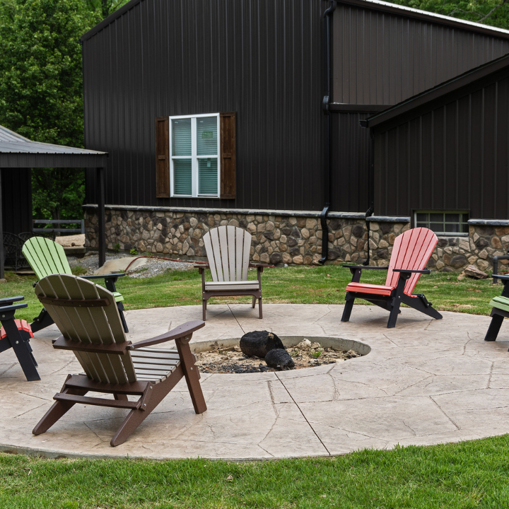 Adirondack chairs around a stone fire pit on a patio beside a dark house with a stone foundation