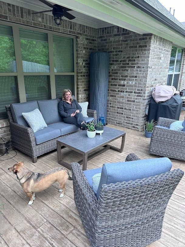 Covered patio with gray wicker seating, coffee table, and a woman sitting beside a dog.