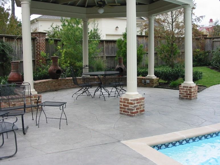 Patio with gazebo, black metal tables and chairs, brick columns, and a swimming pool edge nearby.