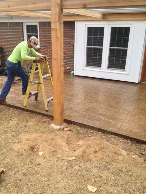 Person on step ladder working on a wooden porch beside white double doors.