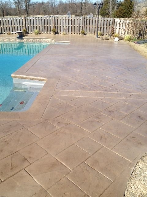 Poolside concrete deck with tan stamped pattern beside blue water and a wooden fence.