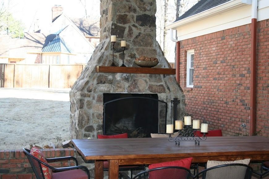 Outdoor stone fireplace beside a wooden patio table and chairs in a backyard