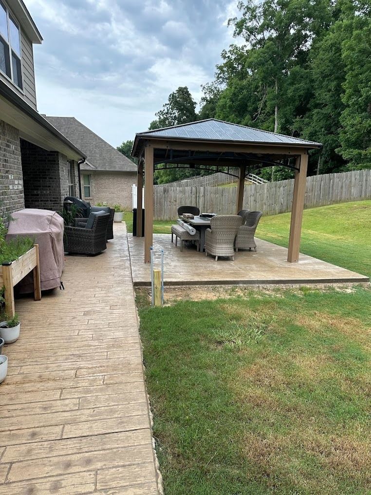 Backyard patio with gazebo, grill, and seating beside a house and grassy yard