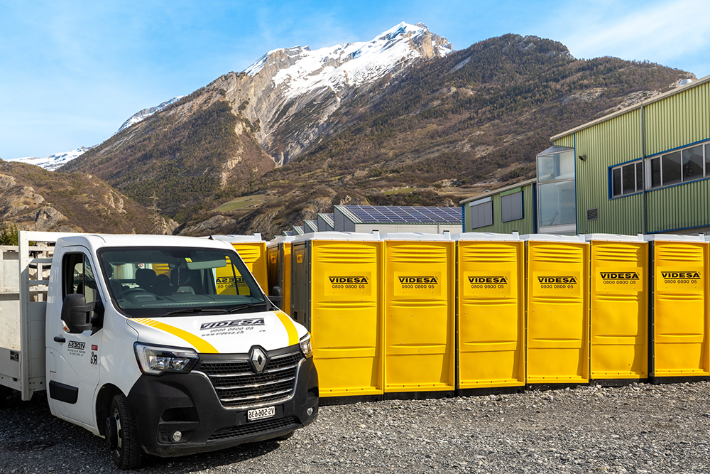 Une camionnette blanche est garée à côté d'une rangée de toilettes portables jaunes.