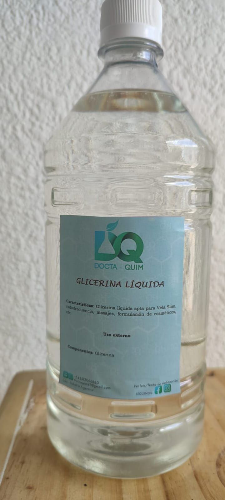 Un líquido transparente en una botella de plástico con una etiqueta azul verdosa, sobre una superficie de madera.