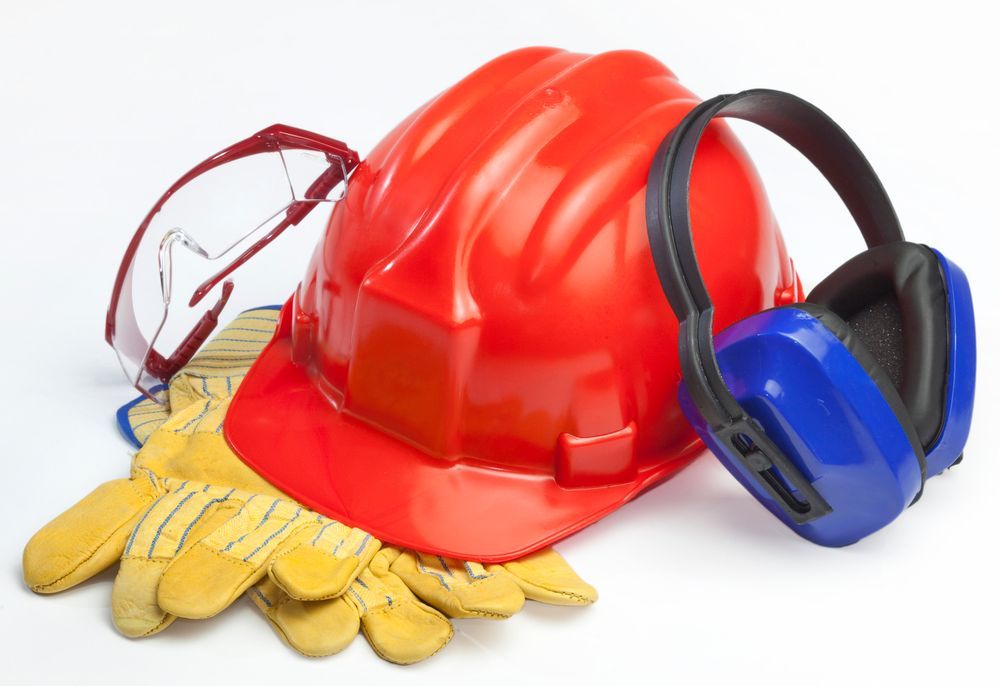 Casco de obra rojo con gafas de seguridad, protectores auditivos azules y guantes de trabajo amarillos sobre fondo blanco