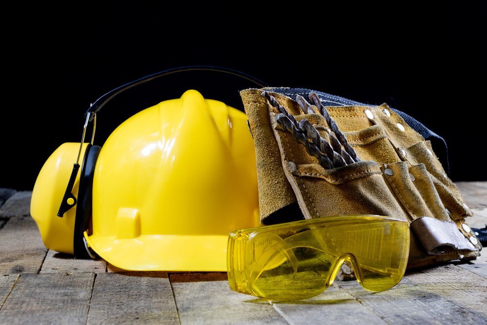 Casco amarillo, guantes, orejeras y gafas de seguridad sobre una superficie de madera, con un fondo negro
