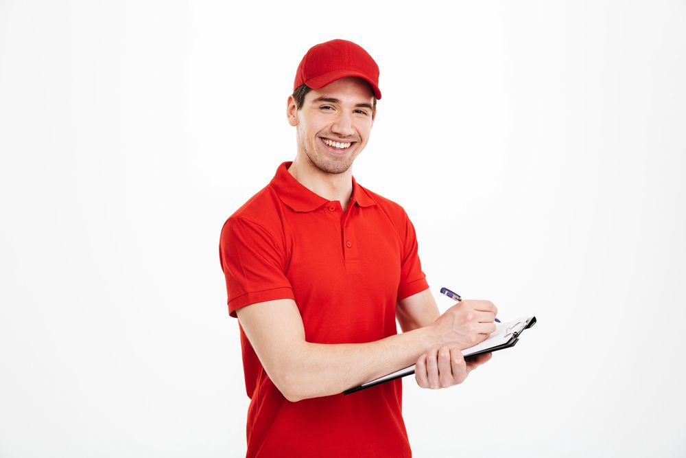 Repartidor sonriente con uniforme rojo, portapapeles y bolígrafo, sobre un fondo blanco