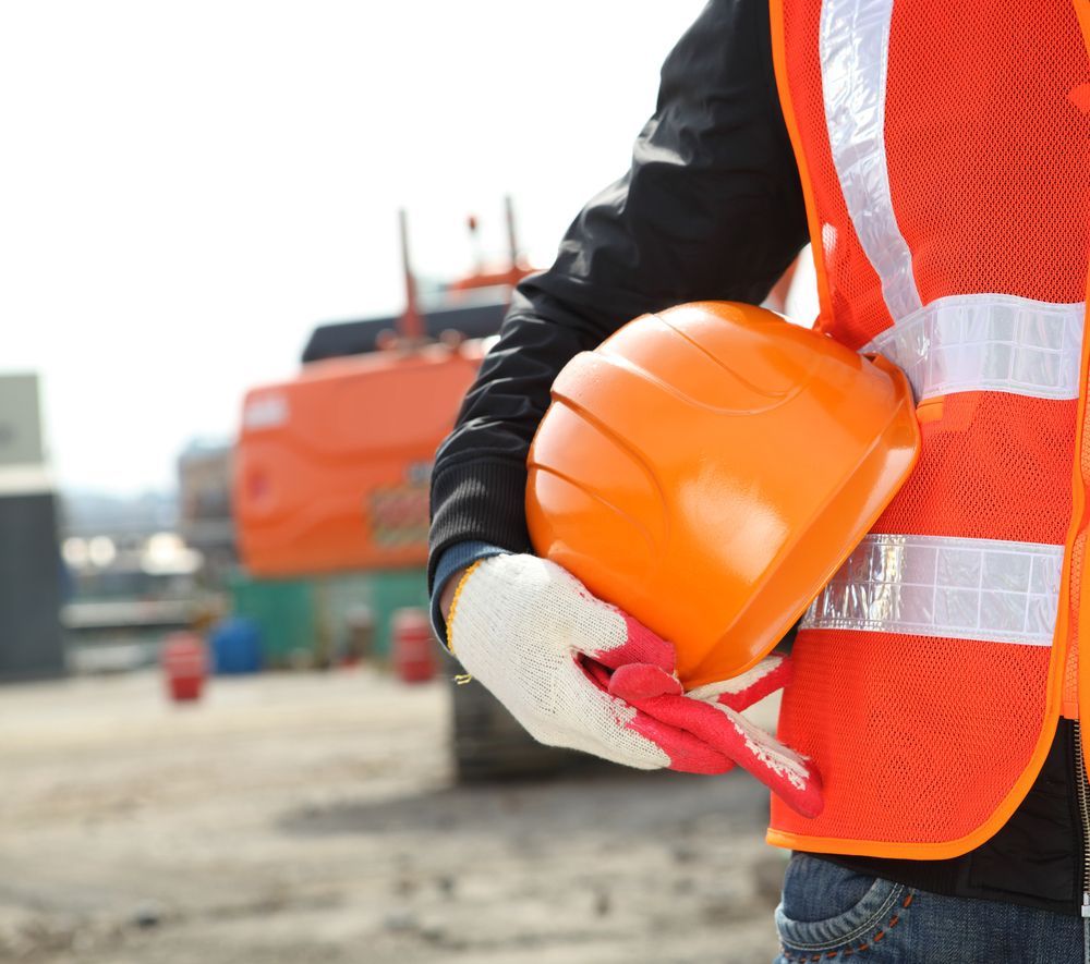 Trabajador de la construcción con un casco naranja en la mano en una obra, con un chaleco reflectante de seguridad