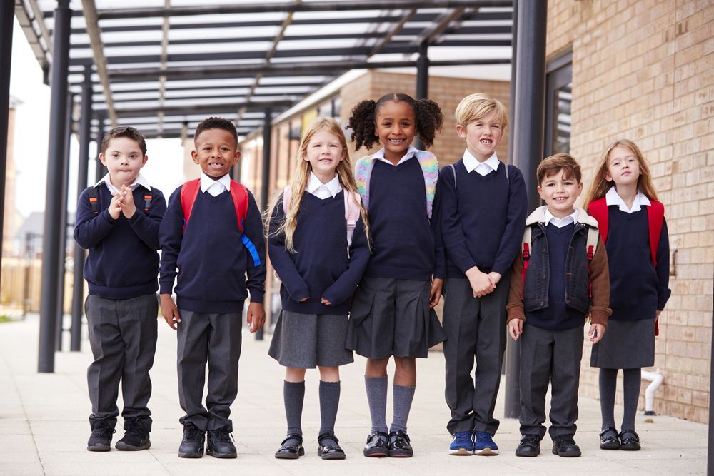 Seis escolares con uniforme están juntos bajo un pasillo cubierto, en el exterior de una escuela.