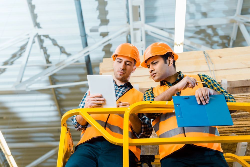 Dos obreros de la construcción con cascos naranjas revisan unos planos en una tableta en una obra.