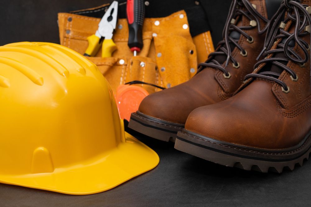 Casco amarillo, guantes de trabajo y botas de seguridad marrones sobre una superficie oscura
