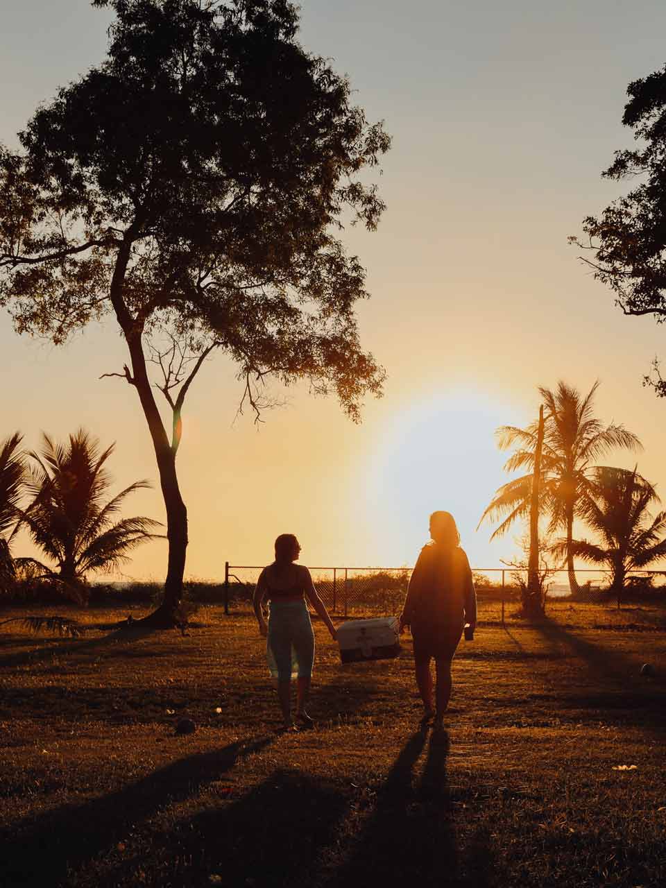 Silhouette at sunset of two young woman carrying an esky