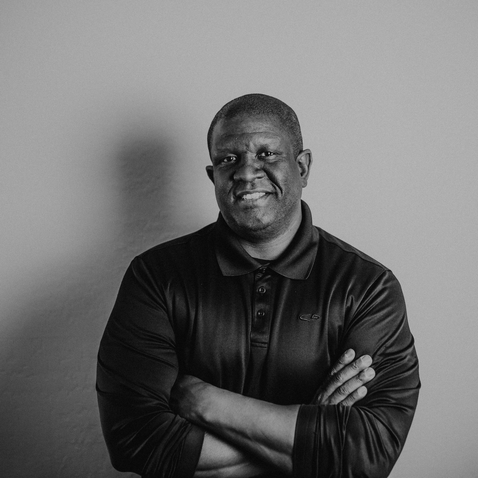 Smiling man in a dark shirt with arms crossed against a plain gray background