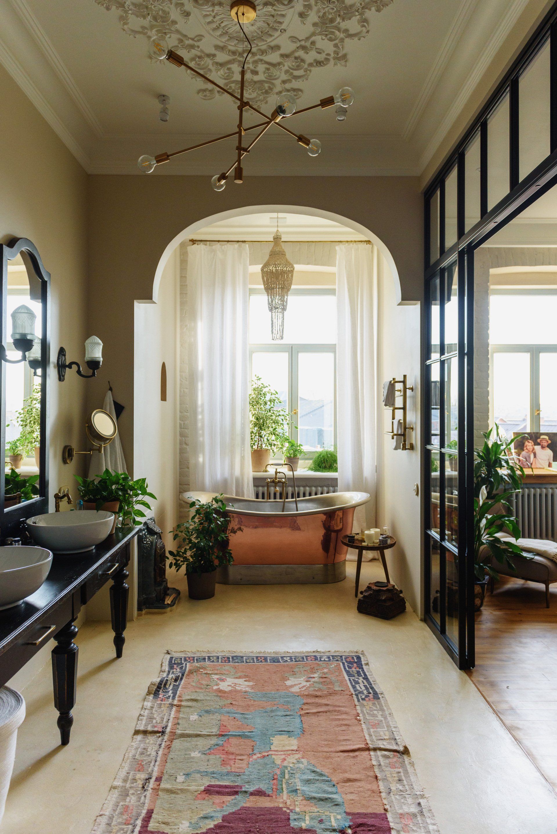 Elegant hallway with black-framed glass doors, patterned runner rug, and a bright archway leading to a room beyond