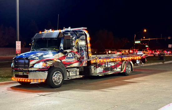 Tow truck with American flag design and lights on at night.