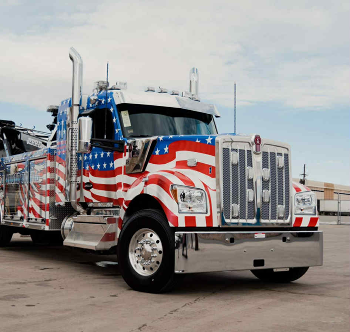 American flag-painted tow truck, Kenworth model, parked on pavement.