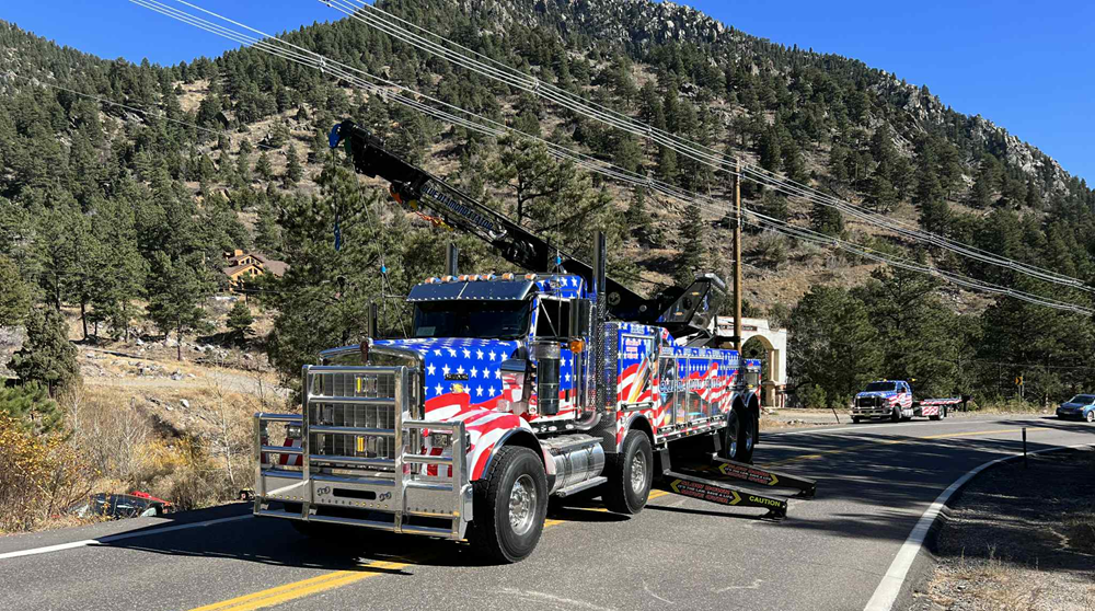 Tow truck decorated with American flag design on a mountain road.