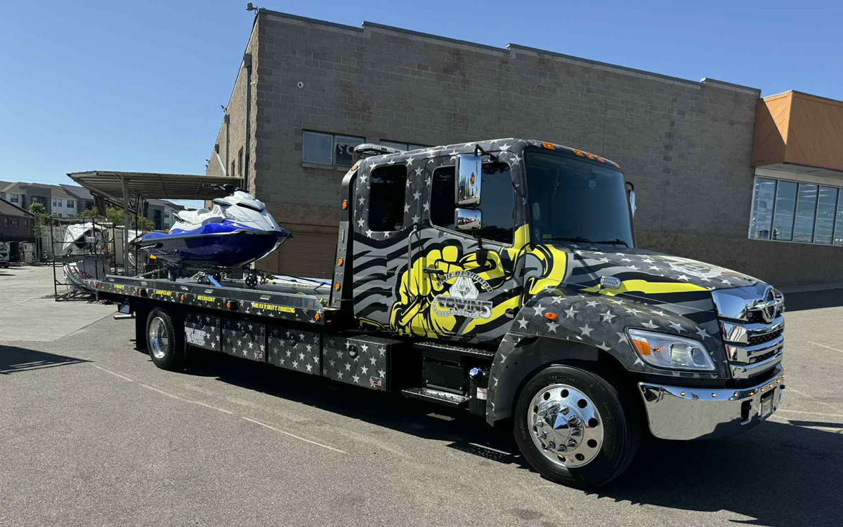 Tow truck with patriotic graphics transporting a blue jet ski.
