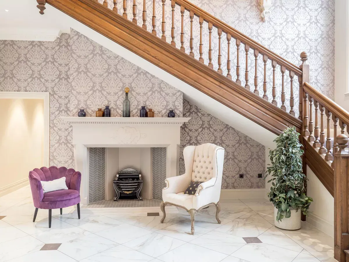 Milverton Hall, A living room with stairs , chairs and a fireplace.