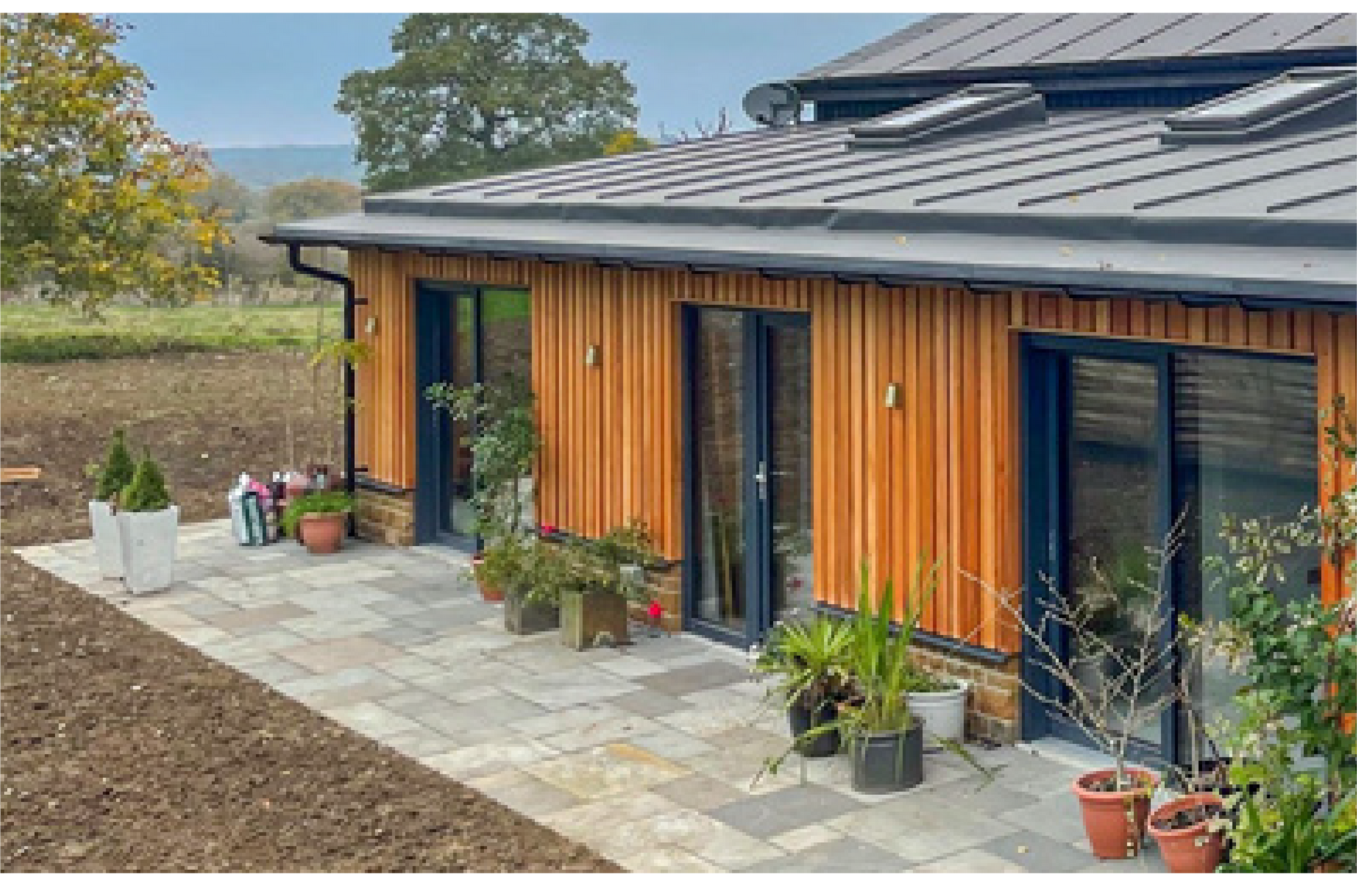 Kingfisher Barn, A wooden house with a metal roof and a patio in front of it.