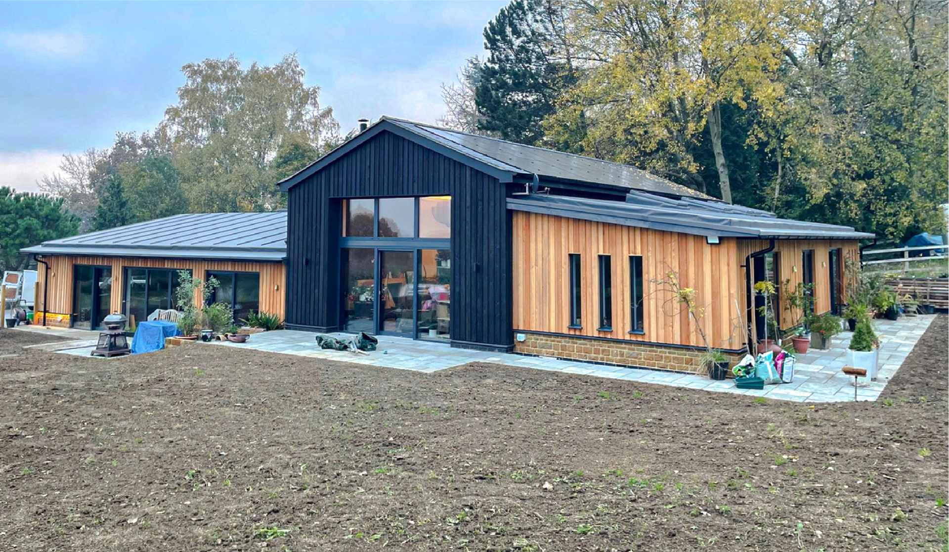 Kingfisher Barn, A large house with a lot of windows is sitting on top of a dirt field.