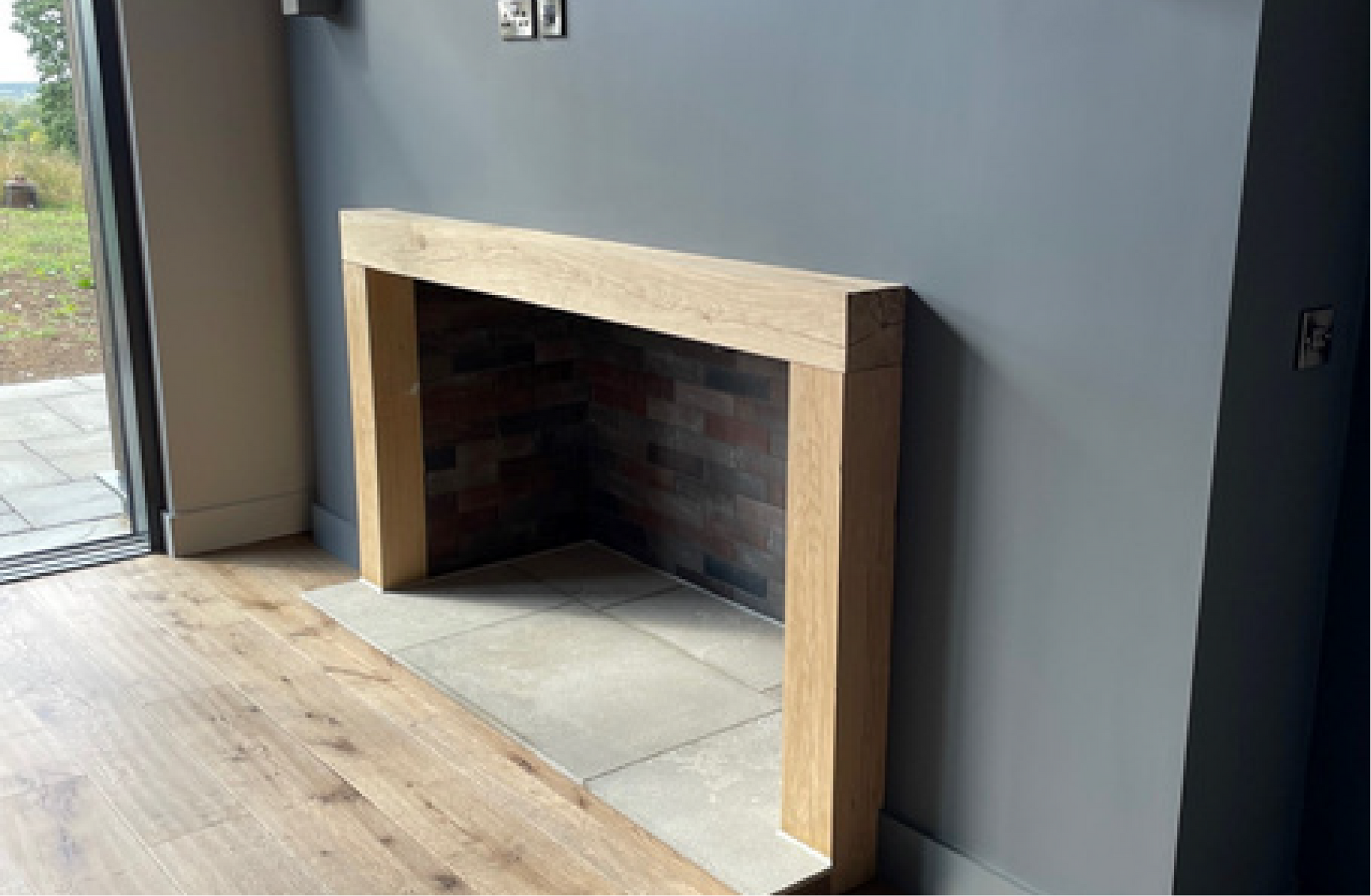 Kingfisher Barn, A fireplace in a living room with a wooden frame and a brick wall.