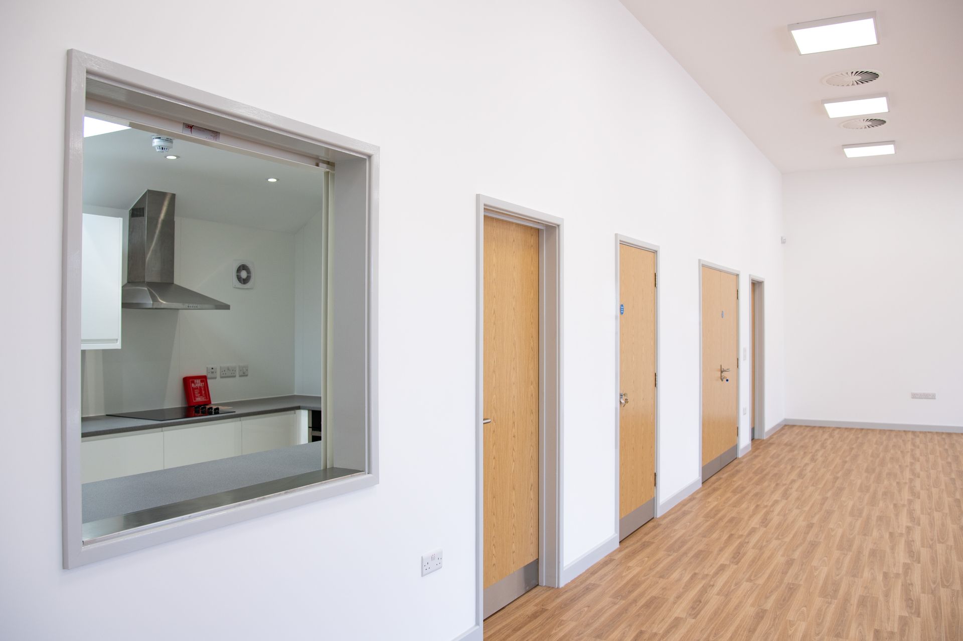 Old School Community Room, A long hallway with a window in the middle of it leading to a kitchen.