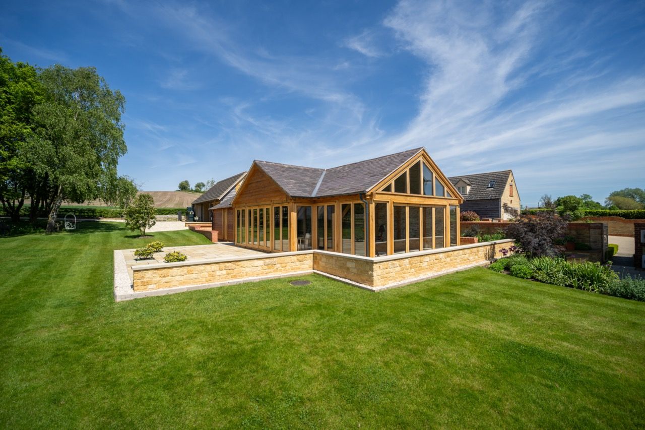 St Dennis Pool House, a large house with a lot of windows is sitting on top of a lush green lawn.