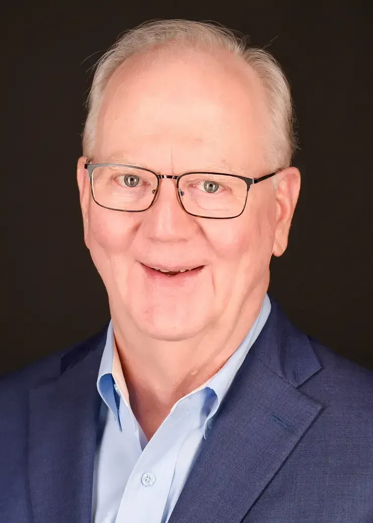 Smiling man in glasses wearing a blue blazer against a dark background