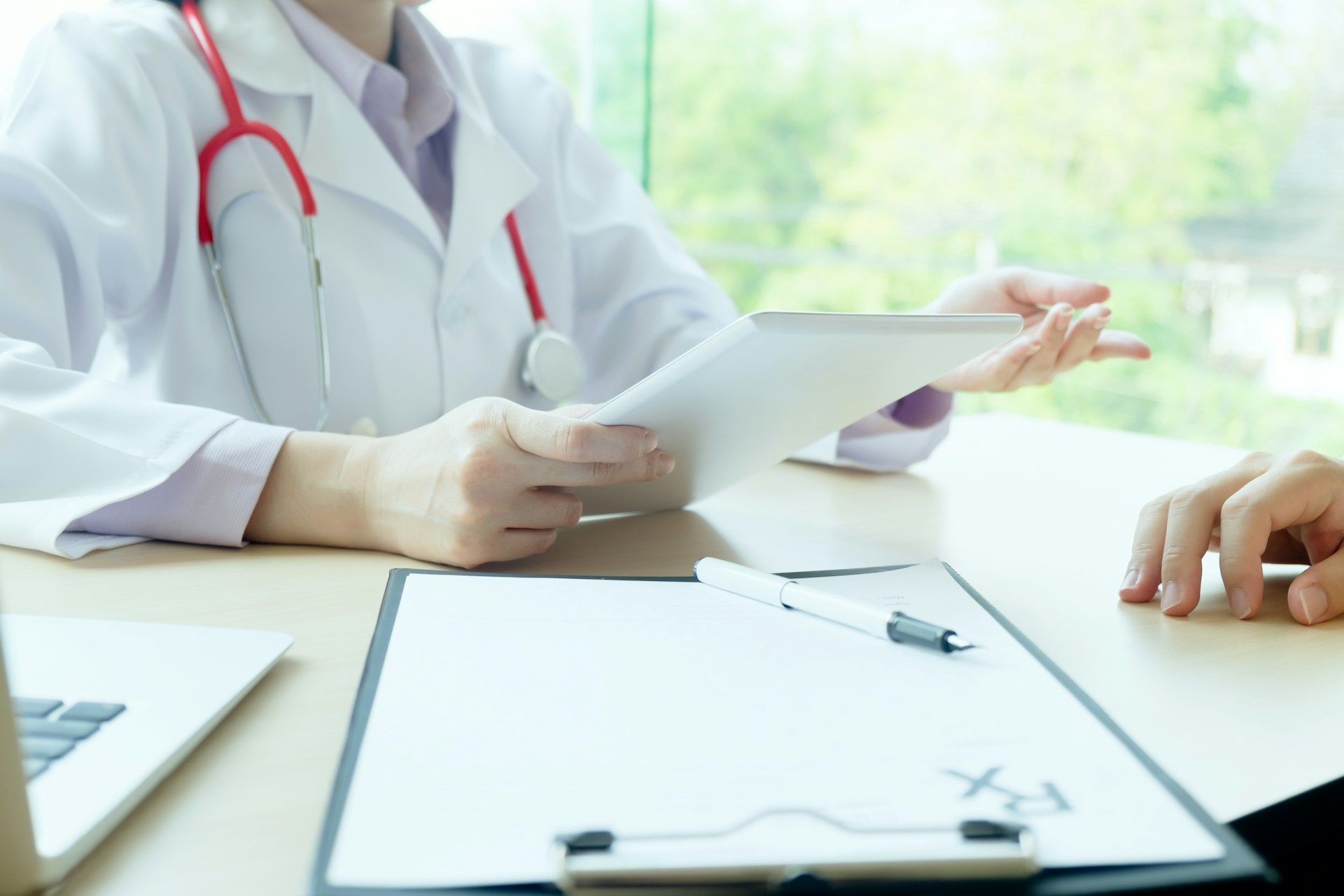 Doctor reviewing documents with a patient at a desk, stethoscope visible, bright clinic setting.