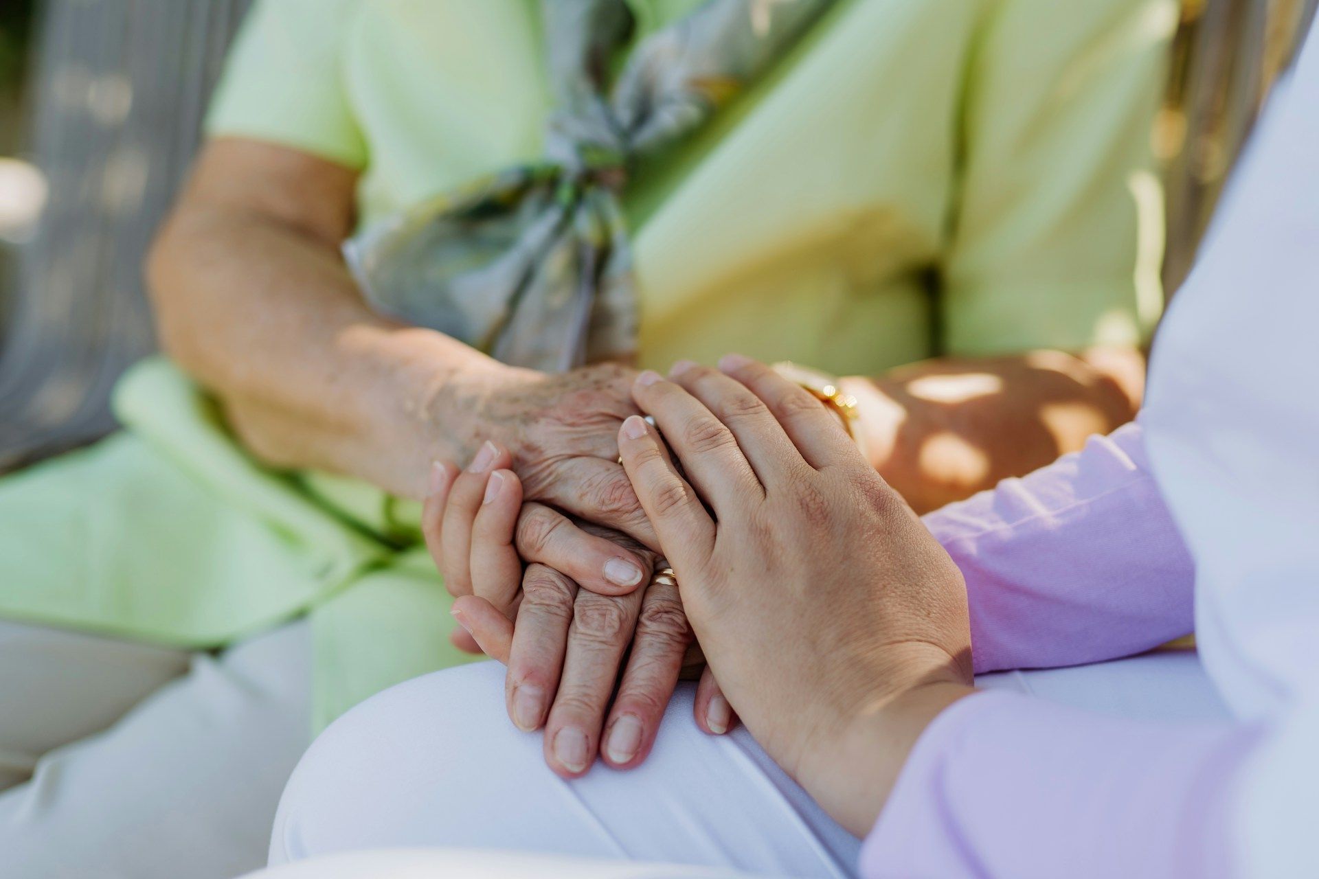 Two people holding hands in a caring gesture, seated together in soft light.