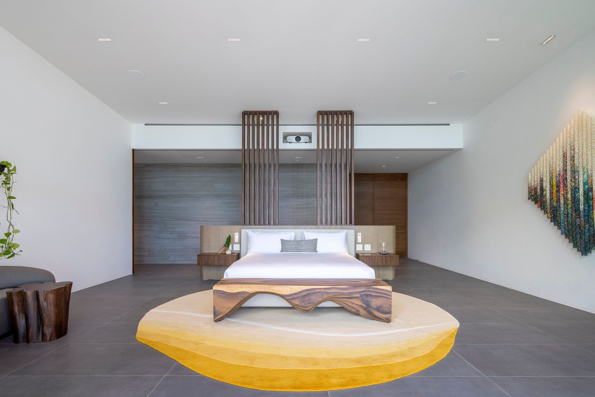 Bedroom with a king-sized bed, wooden accents, and a yellow rug on a gray tiled floor.