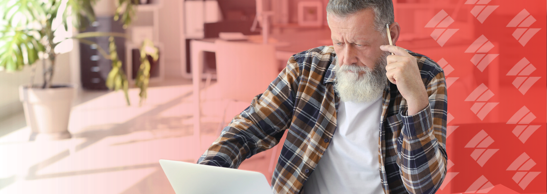 a man with a beard is sitting in front of a laptop computer talking on a cell phone .