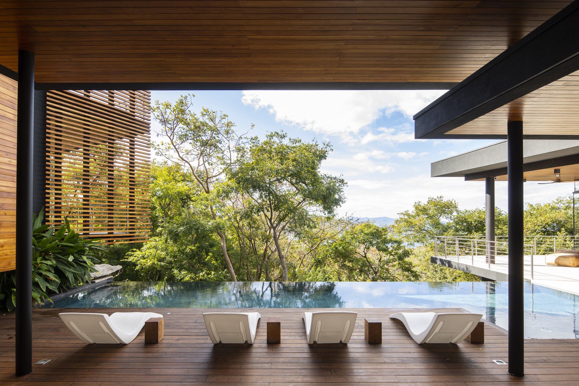 a swimming pool is surrounded by trees and a wooden deck with chairs .