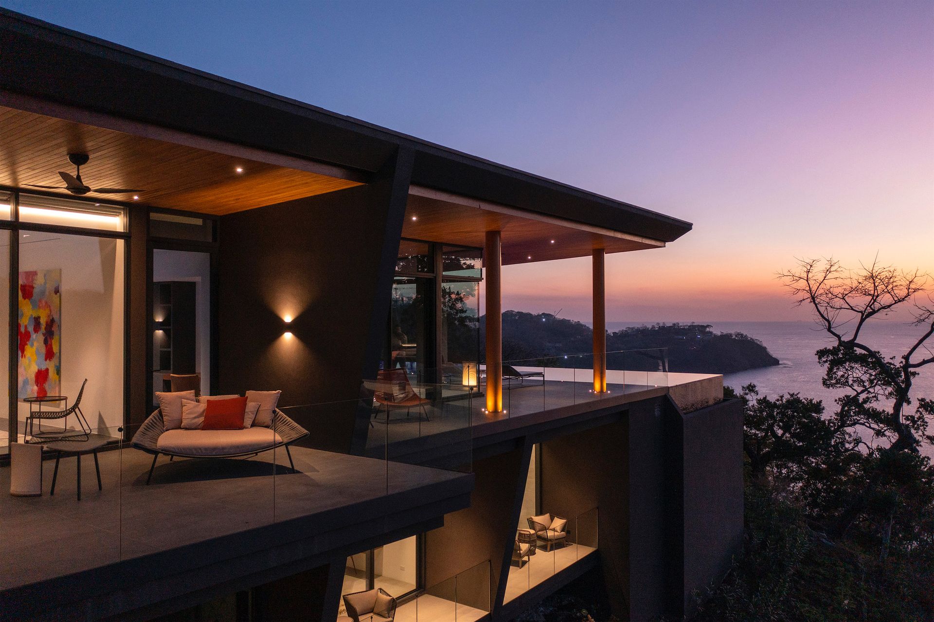 a modern house with a balcony overlooking the ocean at sunset .
