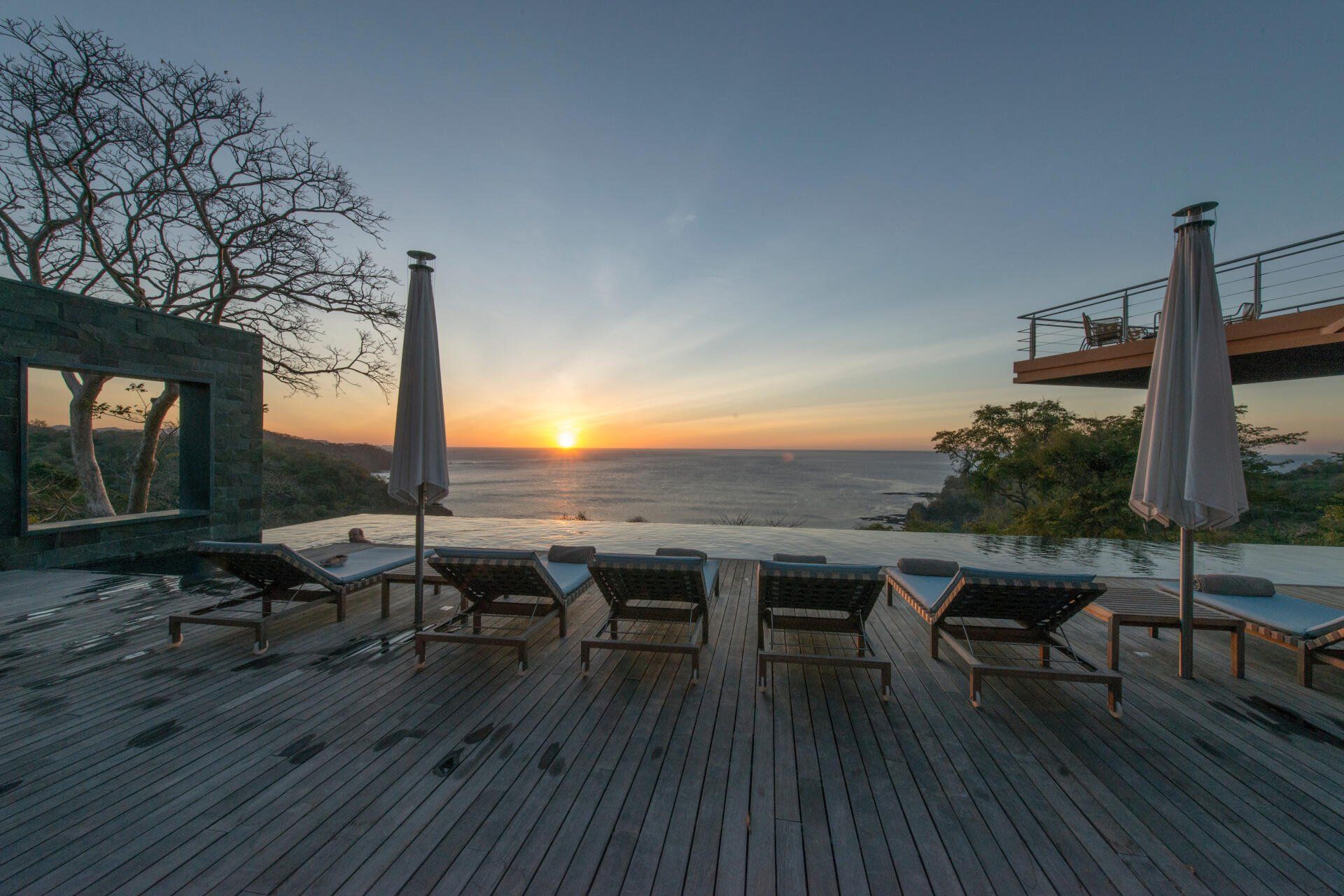 a deck with chairs and umbrellas overlooking the ocean at sunset